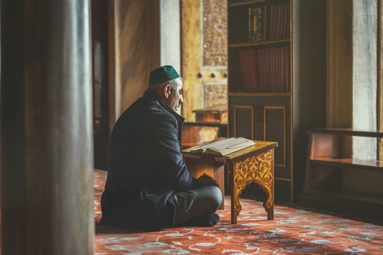 Elderly man reading Koran, seated in a historic Istanbul mosque, reflecting spirituality and contemplation.