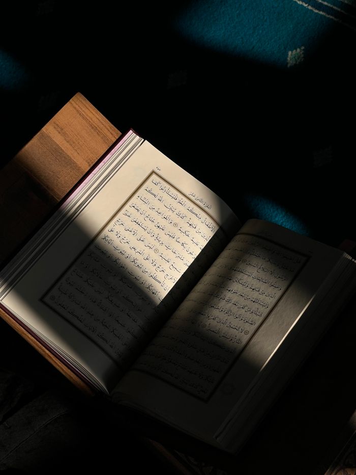 A Quranic book open with sunlight casting shadows, emphasizing spiritual reading.