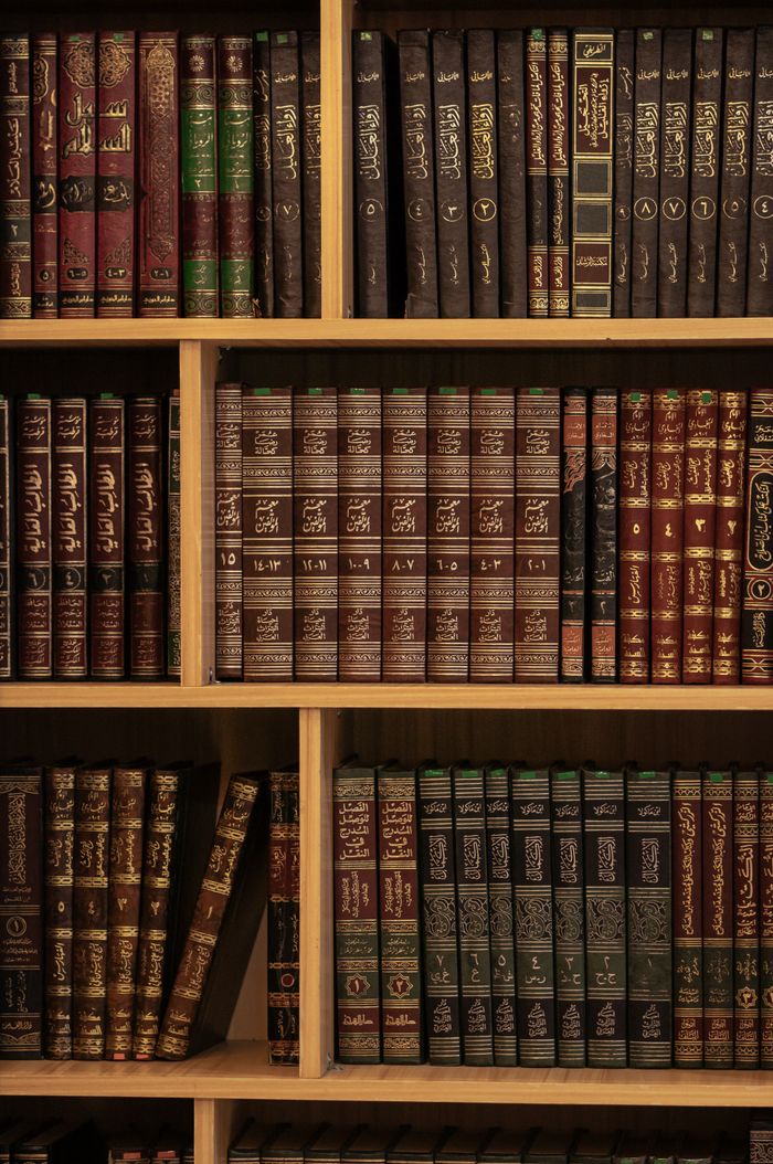 Stack of Islamic religious books neatly arranged on a wooden bookshelf, showcasing vibrant covers with Arabic script.
