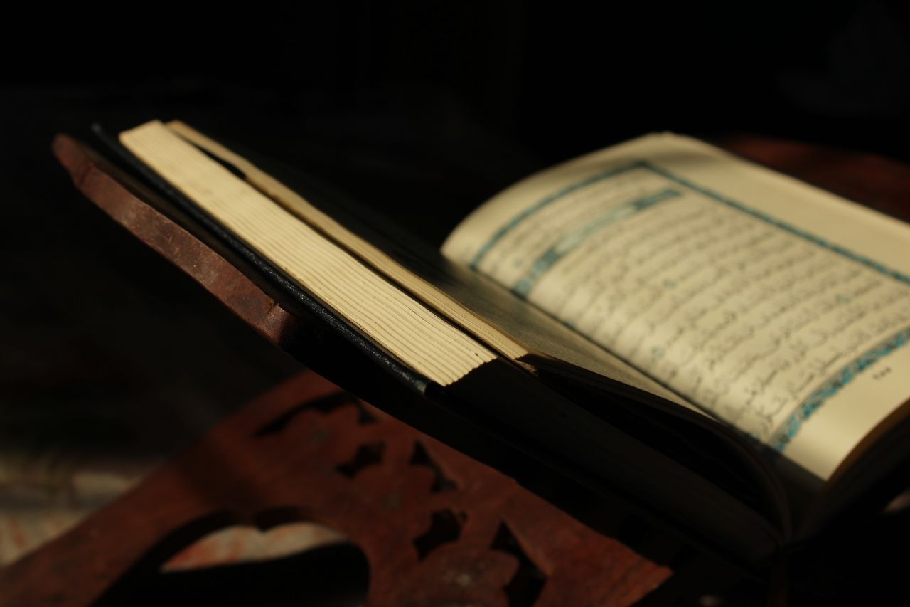 Open Quran resting on a traditional wooden stand, illuminated by soft natural light.