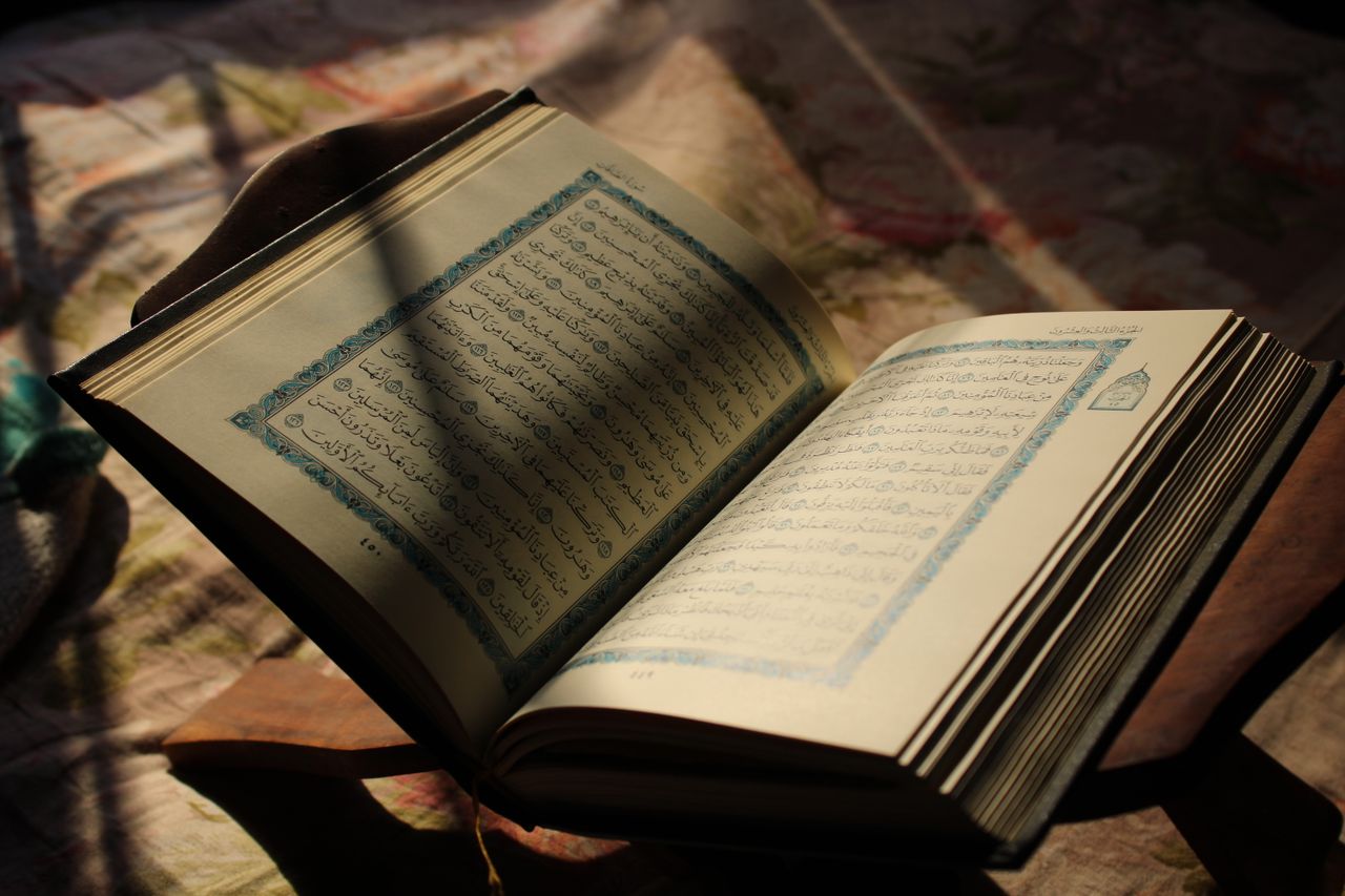An open Quran illuminated by sunlight, placed on a wooden stand, creating a peaceful and spiritual ambiance.